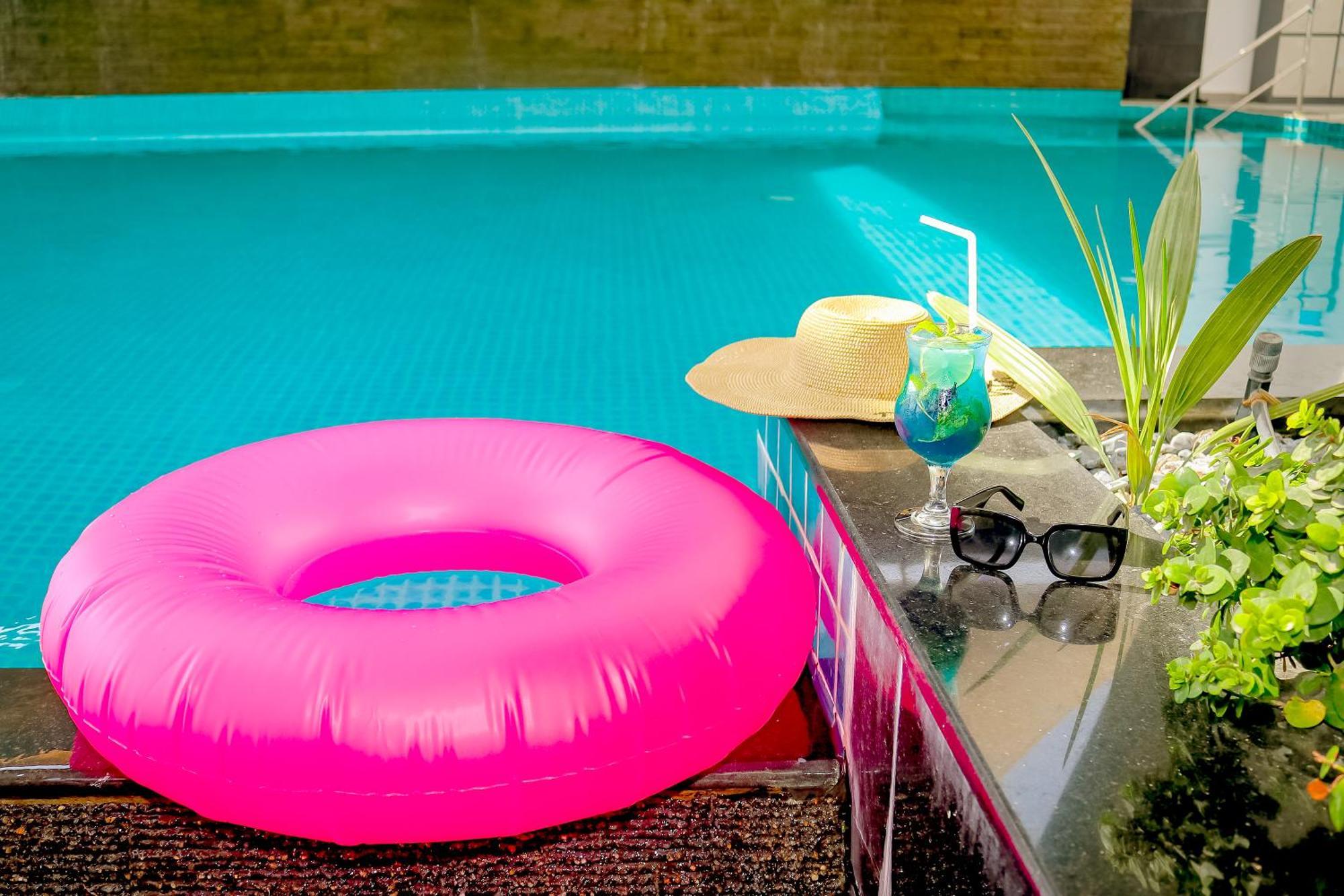 Lagoona Beach Luxury Resort And Spa Al-Manamah Bagian luar foto The photo shows a vibrant and inviting scene by a swimming pool. In the foreground, there is a large pink inflatable float and a stylish straw hat. Next to the float, a refreshing cocktail in a glass is displayed, complete with a straw and garnishes.