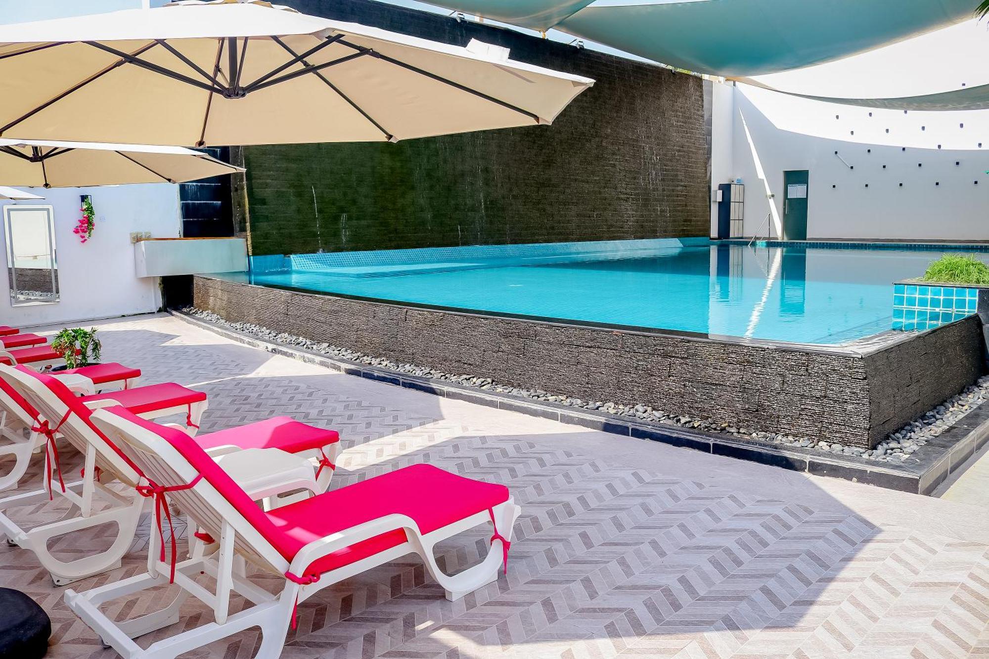 Lagoona Beach Luxury Resort And Spa Al-Manamah Bagian luar foto The photo shows a pool area featuring a rectangular swimming pool with clear blue water. Surrounding the pool are light-colored lounge chairs with pink cushions, positioned under large umbrellas for shade. The pool is bordered by a textured wall, and