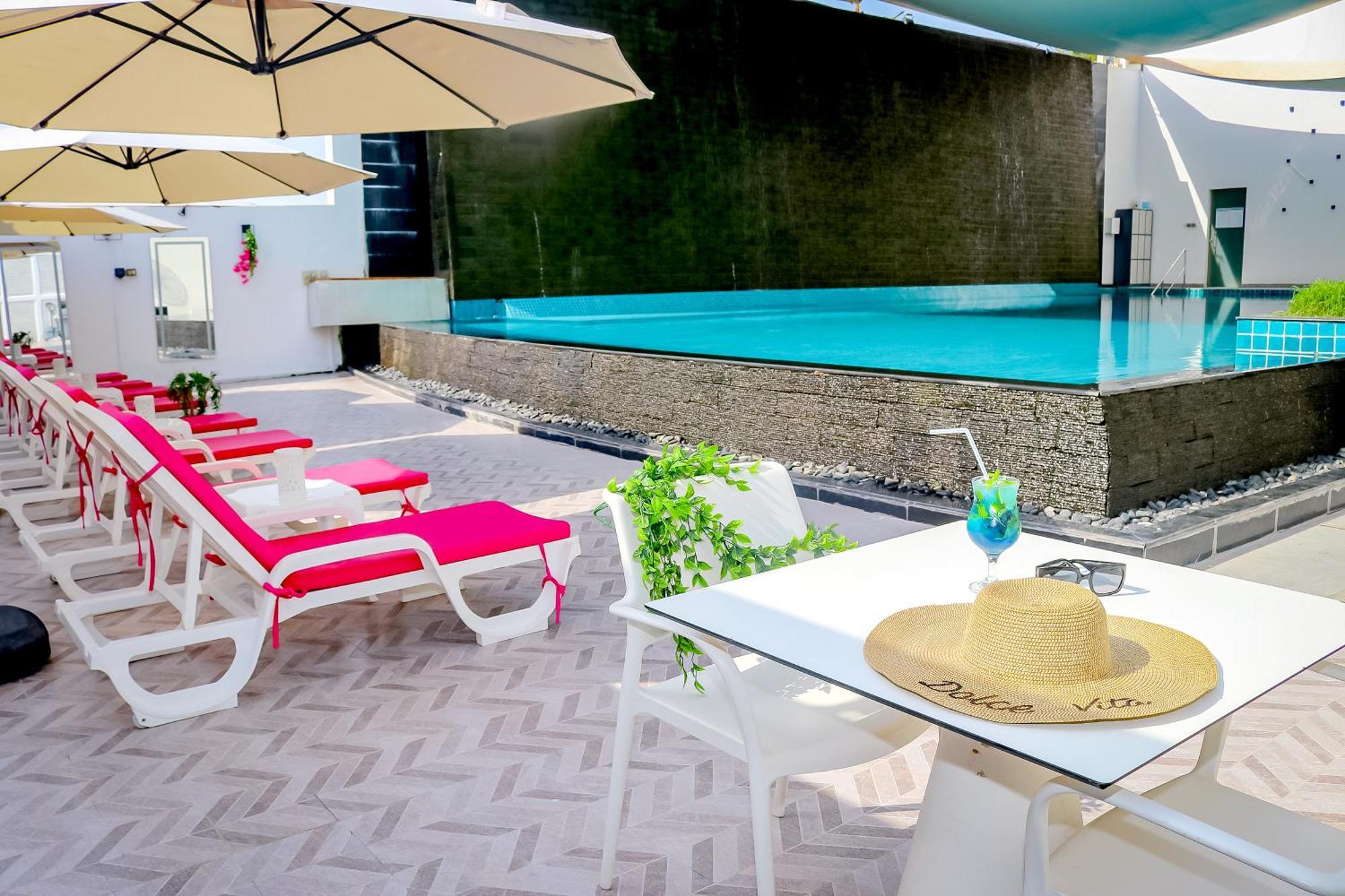 Lagoona Beach Luxury Resort And Spa Al-Manamah Bagian luar foto The photo shows a sunny poolside area with bright red lounge chairs arranged neatly beside a swimming pool. There are large beige umbrellas providing shade. A small table is set up with a straw hat and a colorful drink, suggesting a relaxed, tropical