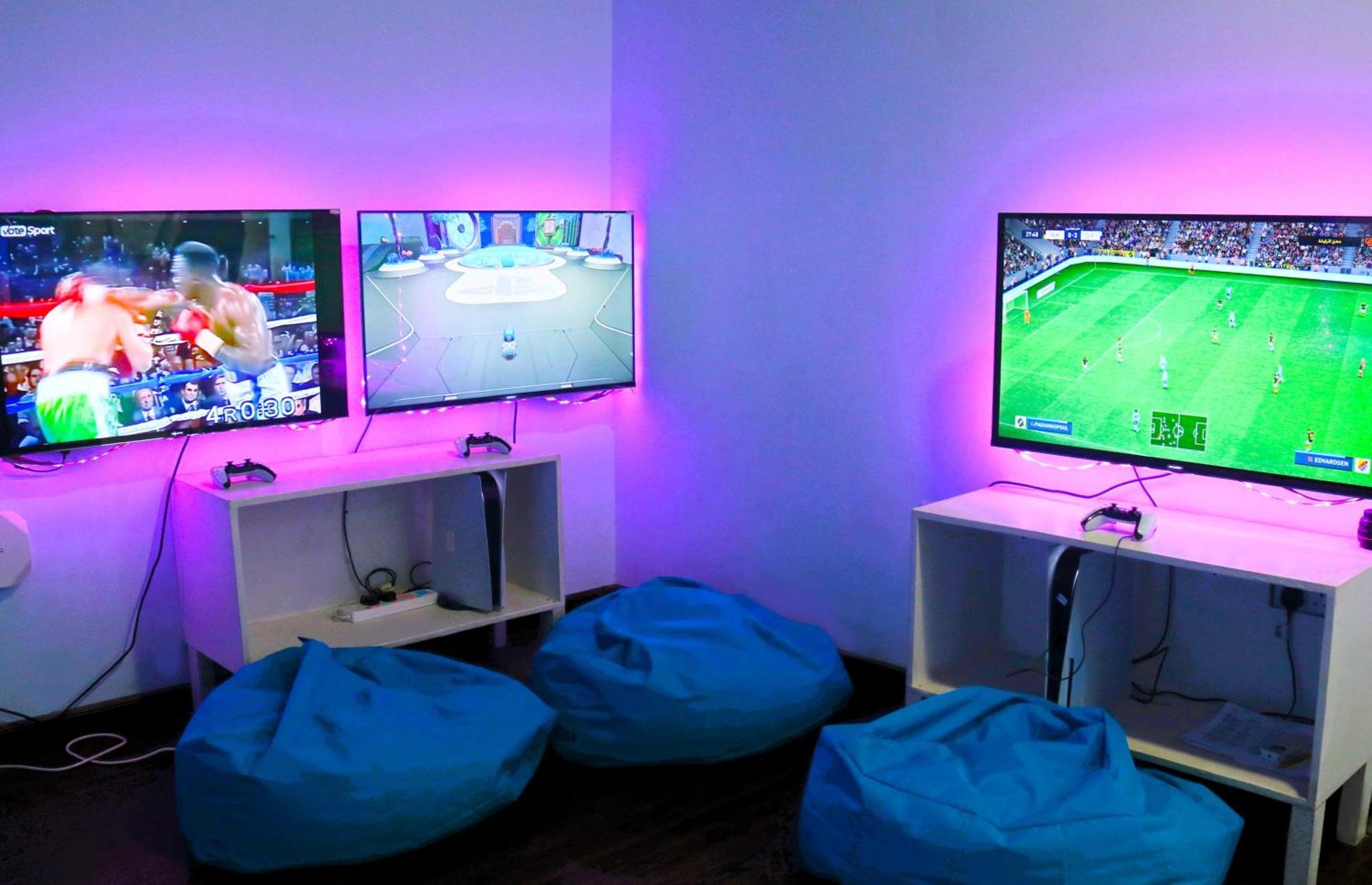 Lagoona Beach Luxury Resort And Spa Al-Manamah Bagian luar foto The photo shows a gaming area featuring three televisions mounted on the wall, displaying different games. Two of the TVs are showing gaming scenes, with one depicting a boxing game and the other showing a vibrant game environment. The third TV displ