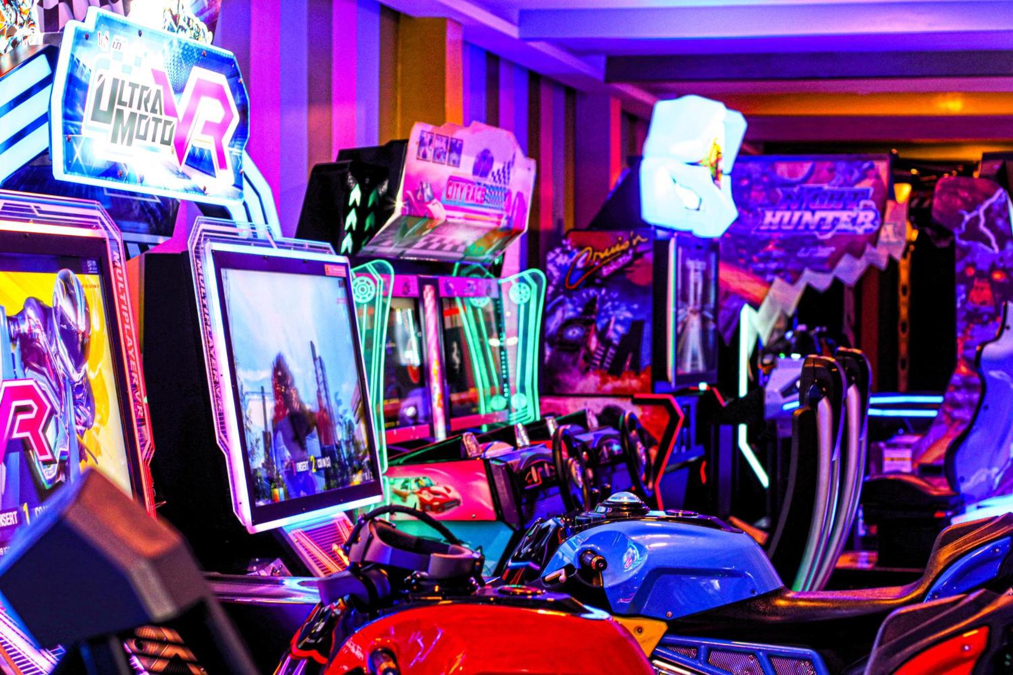 Lagoona Beach Luxury Resort And Spa Al-Manamah Bagian luar foto The photo shows a vibrant arcade scene featuring various arcade gaming machines. The machines are lined up, showcasing colorful screens and bright, neon lights, creating an energetic atmosphere. Some machines appear to be racing games, as indicated b