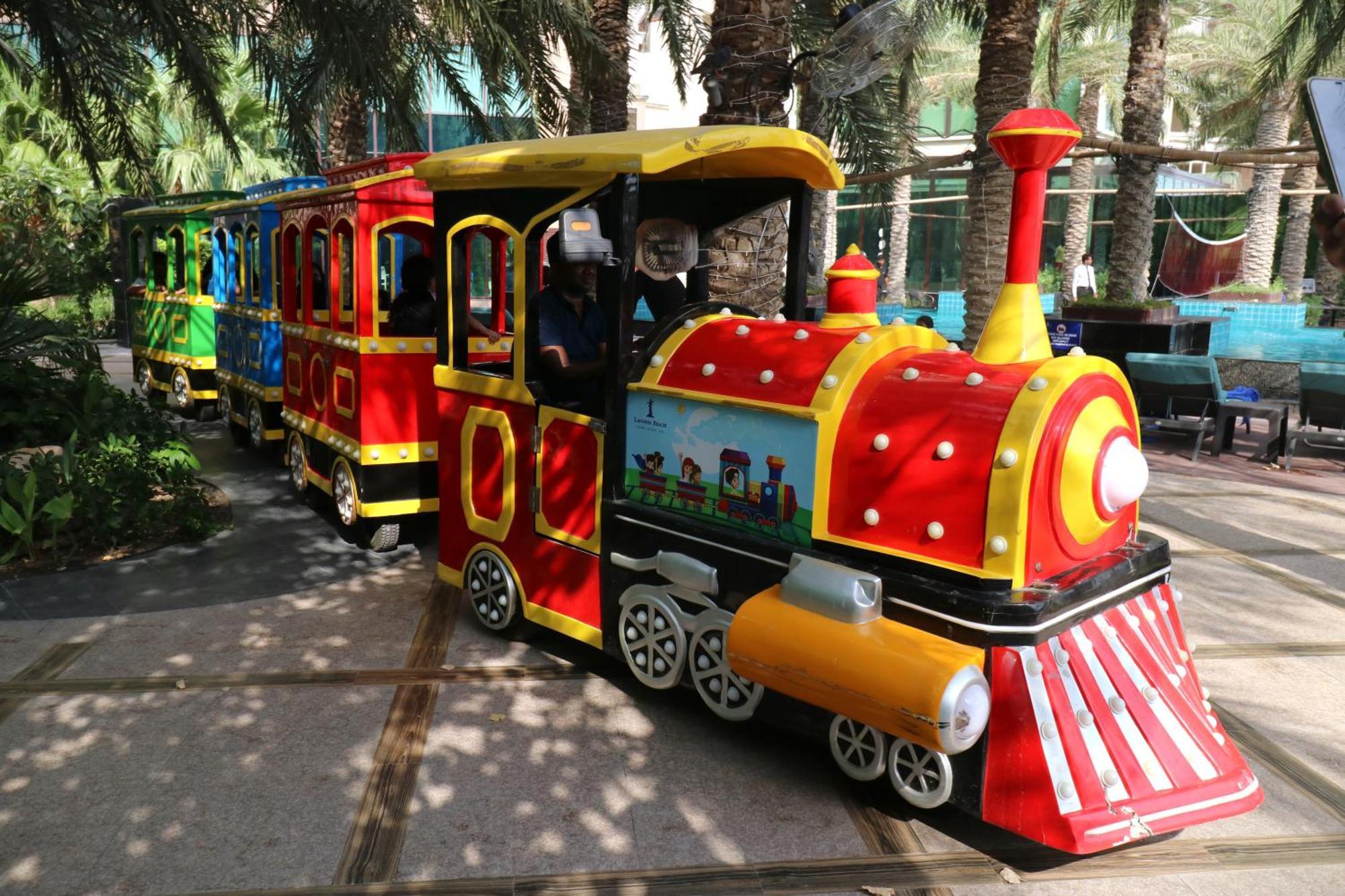 Lagoona Beach Luxury Resort And Spa Al-Manamah Bagian luar foto The photo shows a colorful miniature train. It features a vibrant design with bright red, yellow, and blue colors. The front of the train resembles a classic steam engine, complete with a prominent smokestack. The train is designed to resemble a fun 