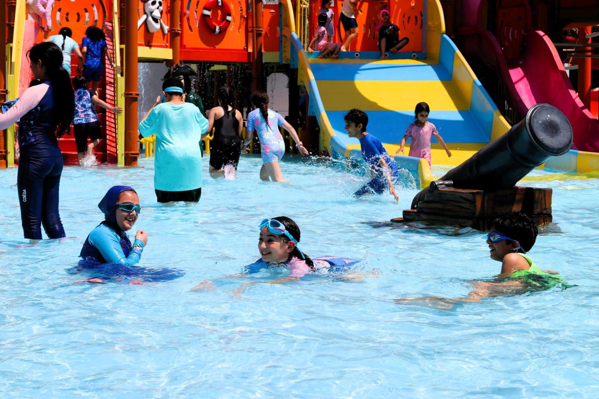 Lagoona Beach Luxury Resort And Spa Al-Manamah Bagian luar foto The photo shows a vibrant water park scene with several children playing in a shallow pool. Some are swimming and splashing around, while others are playing on colorful slides in the background. The atmosphere is lively and cheerful, with kids of var