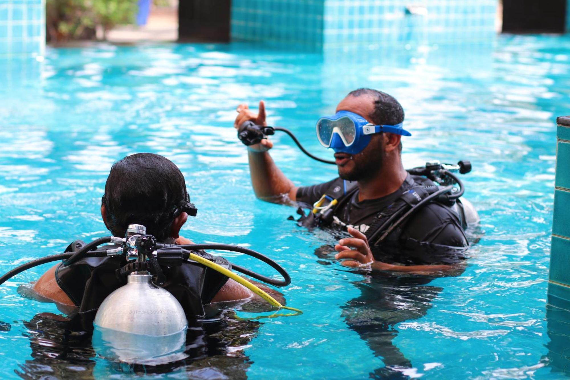 Lagoona Beach Luxury Resort And Spa Al-Manamah Bagian luar foto The photo shows two divers in a pool. One diver is wearing a scuba mask and is speaking to the other diver, who is also equipped with scuba gear. They appear to be engaged in a discussion, possibly related to diving instructions or safety. The water 