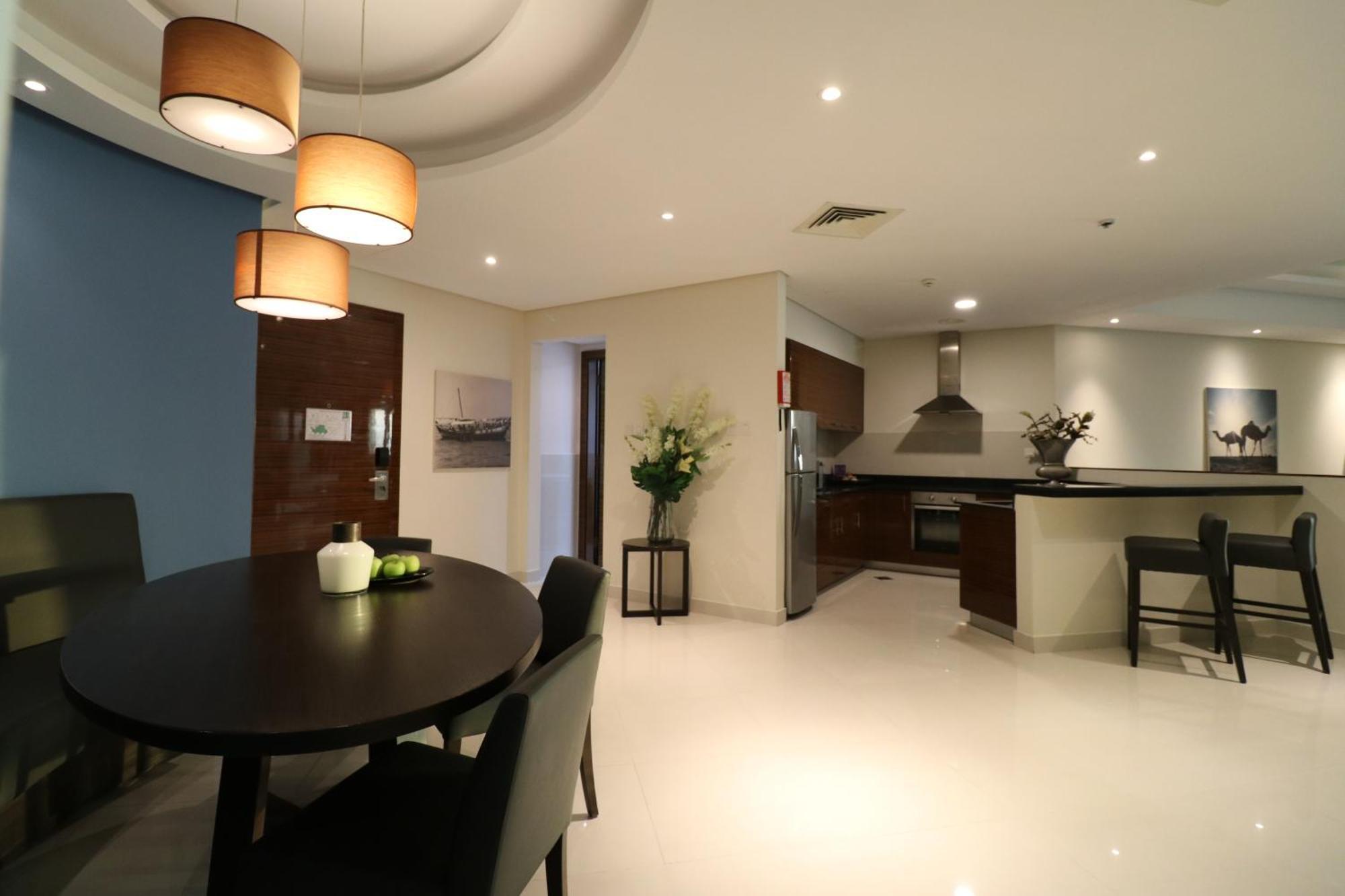 Lagoona Beach Luxury Resort And Spa Al-Manamah Bagian luar foto The photo shows a modern, open-concept dining and kitchen area. On the left, there is a round dining table with black chairs, accompanied by a few decorative elements like a small vase and some fruit. The walls have a combination of light and dark to