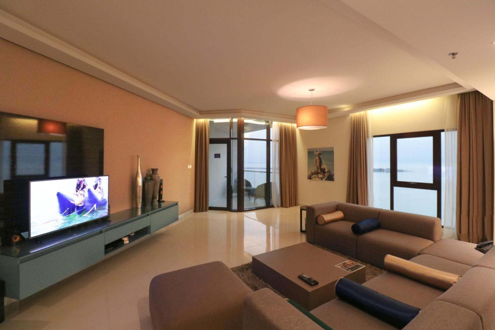 Lagoona Beach Luxury Resort And Spa Al-Manamah Bagian luar foto The photo shows a modern living room with a sleek design. There is a large wall-mounted television on a contemporary entertainment unit, with decorative items placed beside it. The room features a comfortable sectional sofa in light tones, with a cof