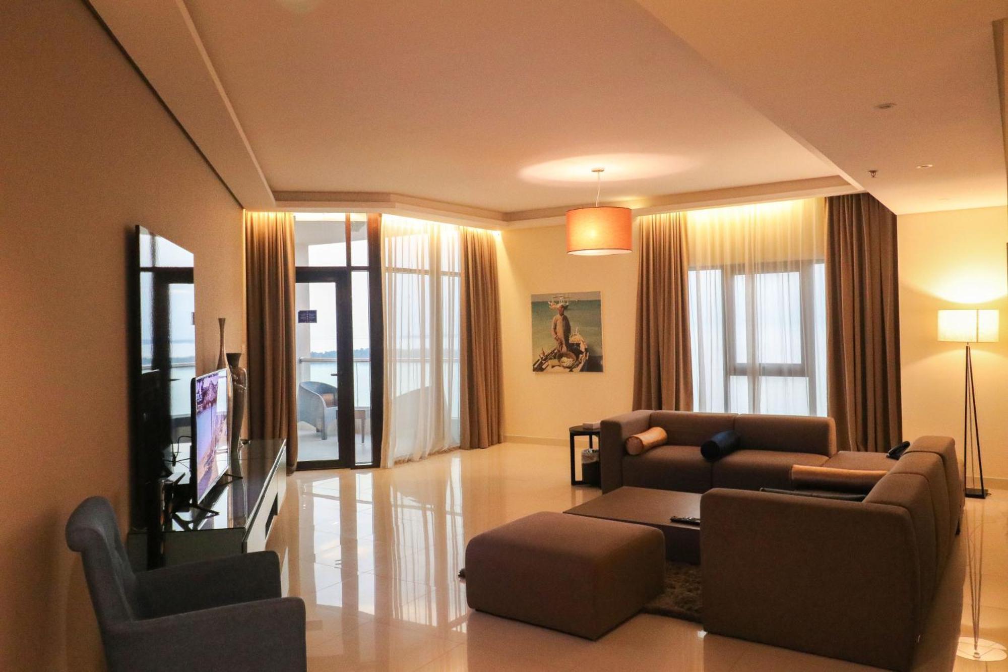Lagoona Beach Luxury Resort And Spa Al-Manamah Bagian luar foto The photo shows a modern living room with a spacious and elegant design. It features a large couch in neutral tones, a soft ottoman, and a stylish coffee table. The walls are painted in a light color, and there are large windows with sheer curtains a