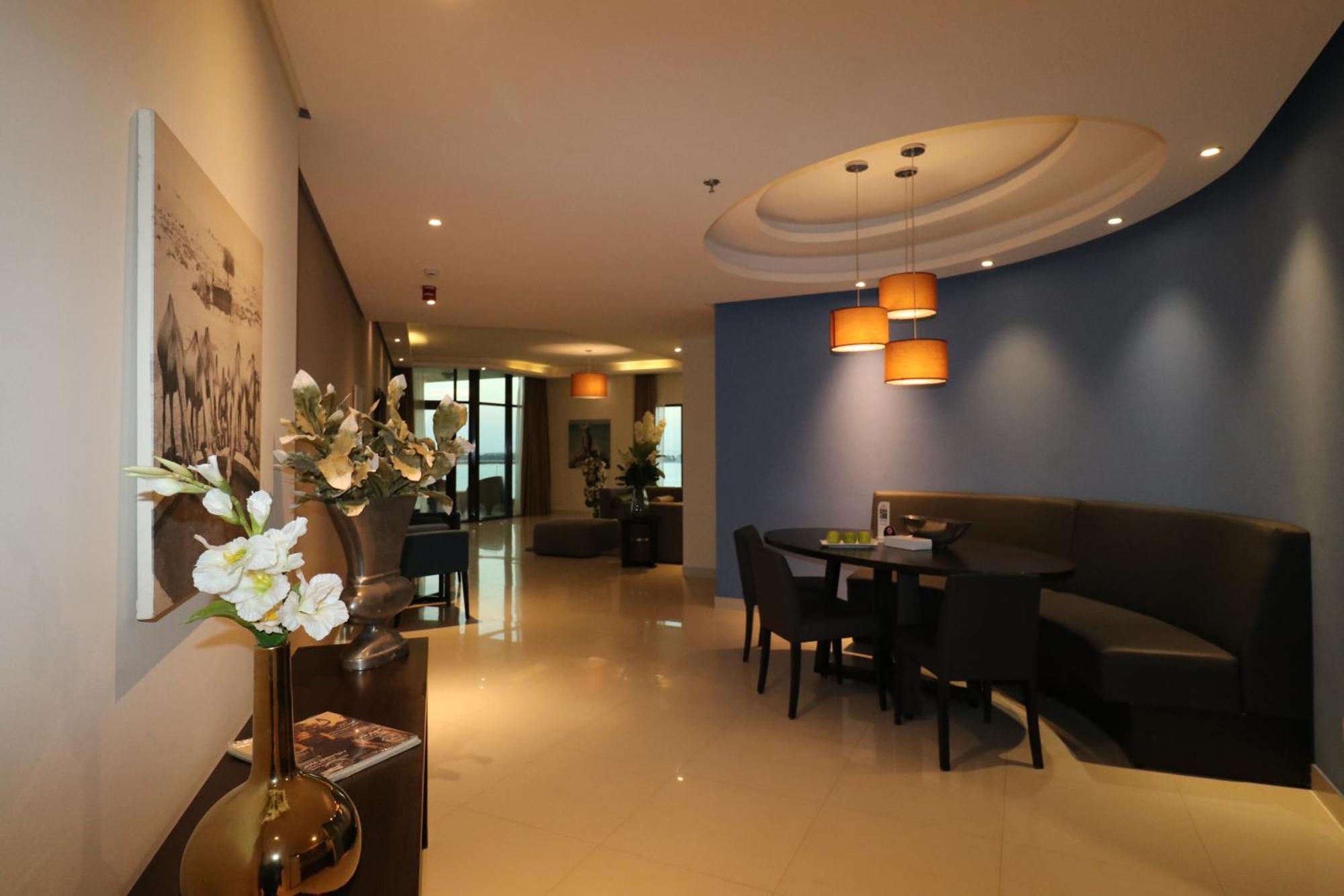 Lagoona Beach Luxury Resort And Spa Al-Manamah Bagian luar foto The photo showcases an interior space, likely a modern lounge or reception area. It features a combination of soft lighting, neutral-colored walls, and decorative elements. There are elegant light fixtures hanging from the ceiling, and a curved blue 