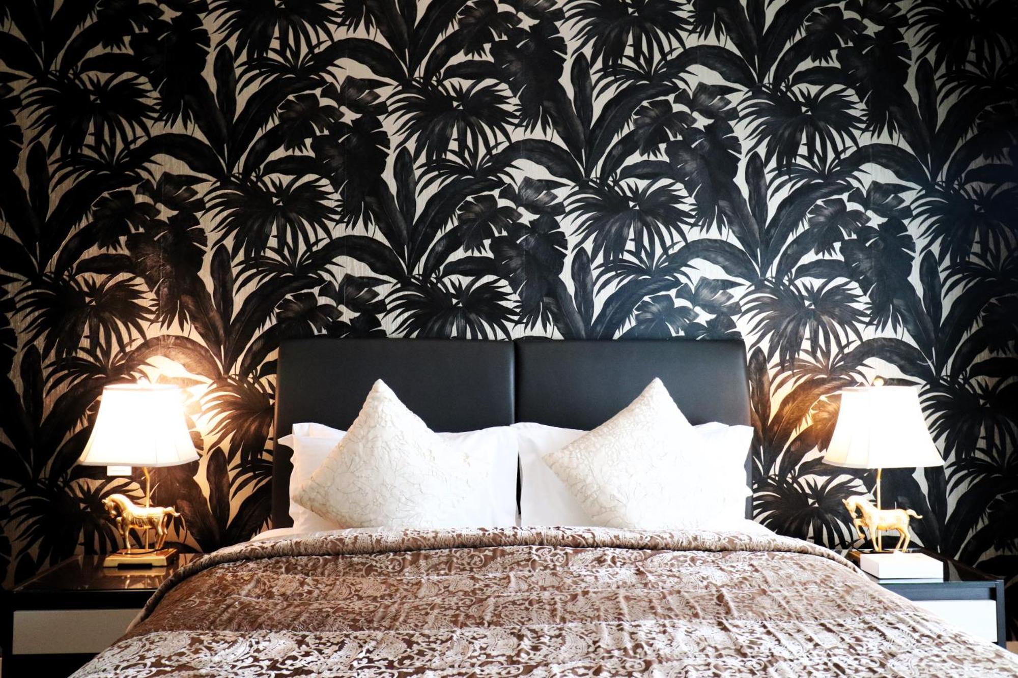 Lagoona Beach Luxury Resort And Spa Al-Manamah Bagian luar foto The photo depicts a stylish bedroom featuring a distinctive wall covered in a black and white tropical foliage wallpaper. The bed has a modern black headboard and is adorned with white pillows, creating a clean and elegant look. A textured brown thro